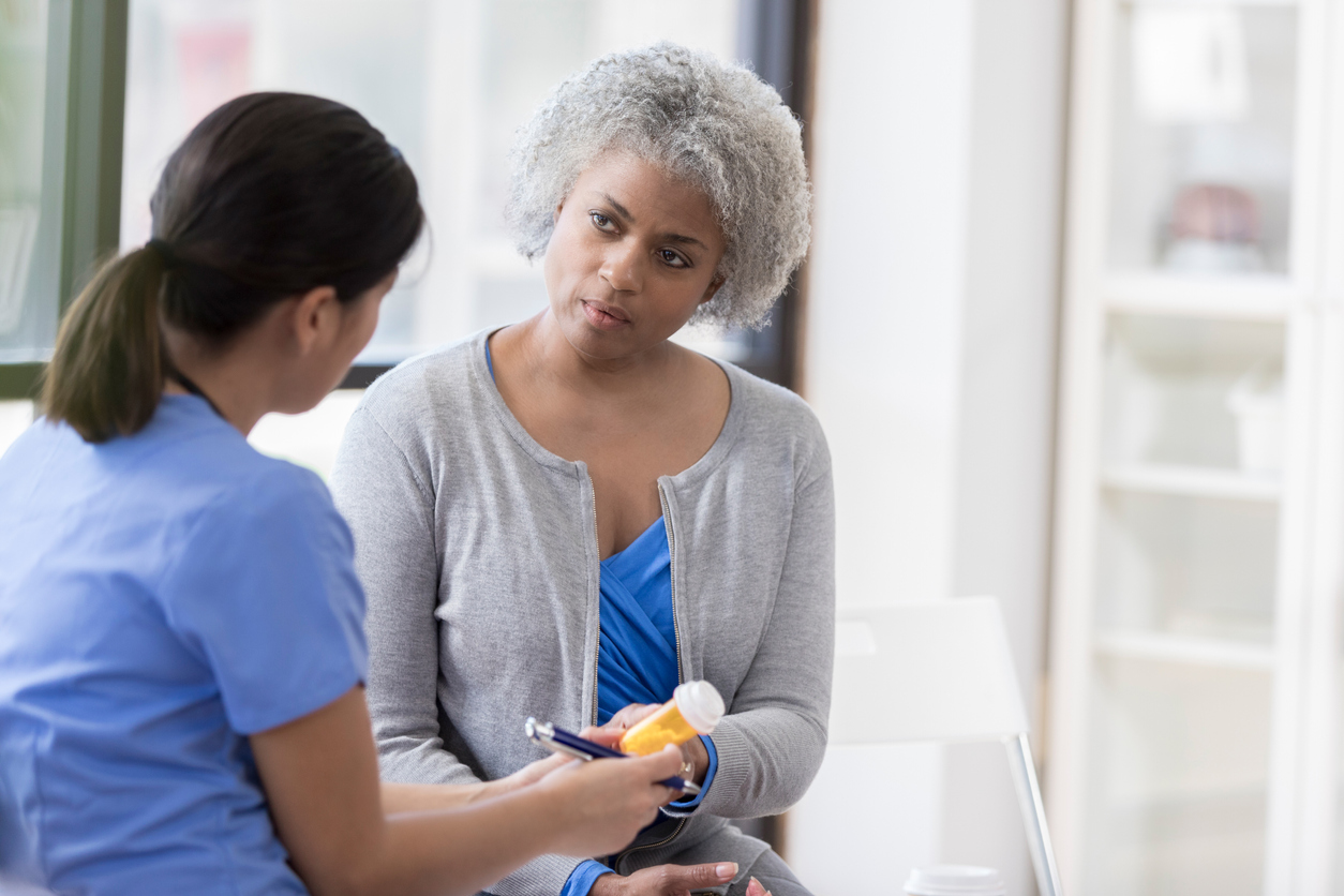 older woman speaking to a doctor who’s holding a prescription bottle